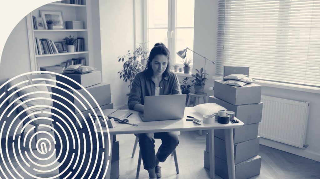 Personne devant un ordinateur portable entourée de boîtes d'expédition empilées dans un espace de travail à domicile